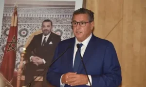 عزيز أخنوش يلقي كلمة حول إنجازات قطاع السياحة المغربي مع خلفية تتضمن صورة للملك محمد السادس والعلم المغربي.